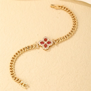 Detail view of gold Cuban chain bracelet featuring a ruby-red clover pendant with zircons