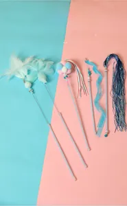 Detail of colorful feather cat wands with bells and glittery sticks on two-tone background