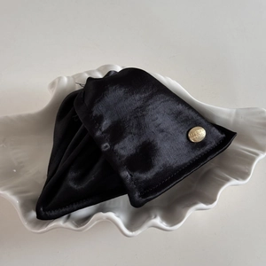 Détail d'une pince à cheveux en satin noir avec badge doré gravé en métal chic