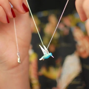 Detail of a blue gradient enamel hummingbird pendant on a silver link chain held by hand
