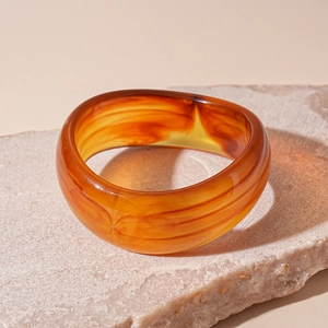 Macro shot of amber resin wide bangle with marble texture on pink natural stone base