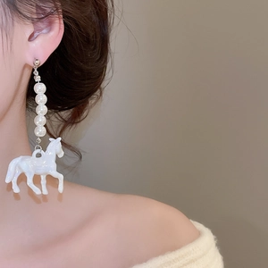 Gros plan d'une boucle d'oreille cheval avec perles blanches portée par un modèle