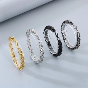 Byzantine chain bracelets in gold, silver, and black stainless steel on a display stand