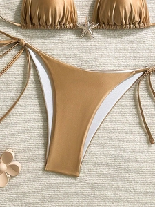 Detalle de bikini dorado con adorno de estrella de strass y lazos laterales en alfombra