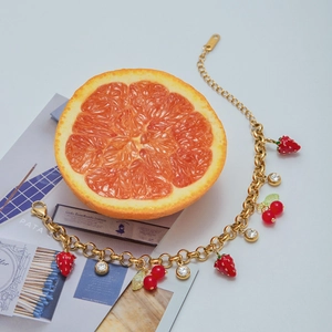 Detail of gold chain bracelet with strawberry pendants and cherries on grapefruit decor