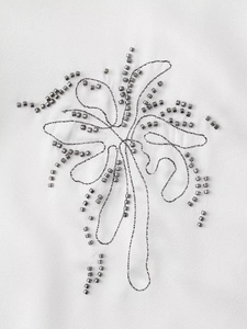 Close-up of gray metal beads and embroidery on white textured fabric for clothing