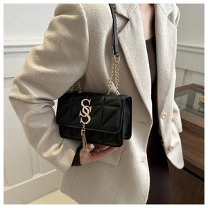 Detail of black quilted shoulder bag with golden S logo and tassel on a model