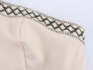 Dettaglio del tessuto in lino beige con bordo geometrico bianco e nero sulla scollatura