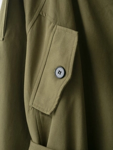Détail du trench-coat vert olive montrant la texture du tissu et les boutons noirs
