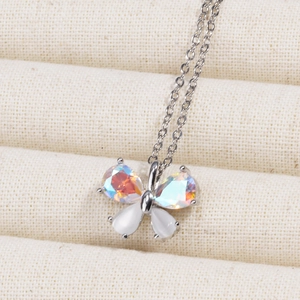 Silver butterfly necklace with rainbow zircons and white opal wings on a beige jewelry pad