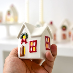 Ceramic Christmas snow house with glowing light and festive wreath held in hand