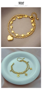 Detail view of gold titanium bracelets with heart and star charms on textured fabric