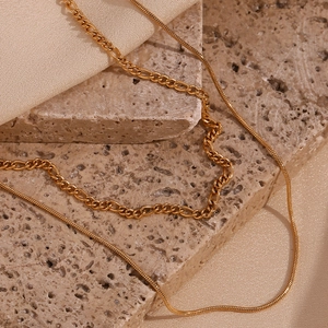 Detail of gold double-layered necklace with sleek snake and textured curb chain links