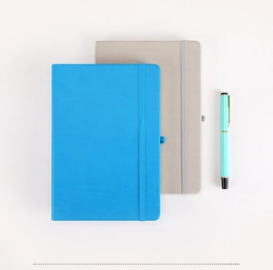Flat lay of A5 leather notebooks in blue and grey with a mint green pen on white background