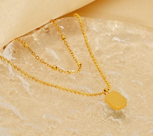 Close-up of double-layer gold titanium necklace with rectangular textured pendant on silk