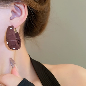 Close-up of a large C-shaped hoop earring with brown fabric and white polka dots pattern