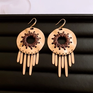 Close-up of golden hollow metal earrings with brown woven rope and long tassel details
