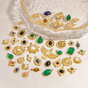 Detailed close-up of mixed gold-plated stainless steel charms with gemstones on marble