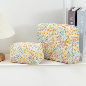 Quilted floral cosmetic bag set including two sizes on a white table with a warm desk lamp