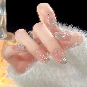 Sparkly glitter gradient press-on nails with small rhinestones on soft white fabric