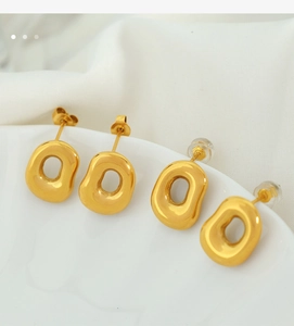 Close-up of four gold irregular hollow earrings with metallic luster on white fabric