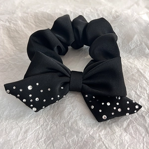 Detail of a black satin bow hair tie with sparkling rhinestone accents on white paper