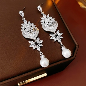 Detail shot of silver heart leaf earrings with sparkling diamonds and round pearls on box