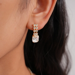 Close-up of elegant gold earrings with emerald-cut crystals worn by a model
