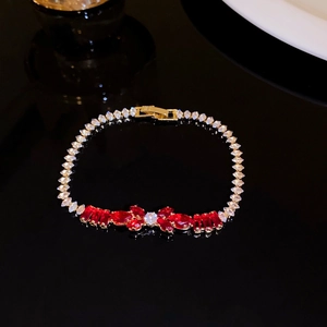 Detail of elegant gold bracelet with red bow-shaped zircon stones on black background.