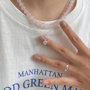 Close-up of minimalist 925 silver ring worn with a heart pendant and pink bead necklace