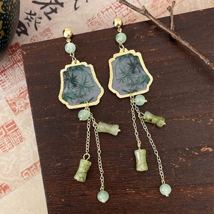 Detail of gold bamboo leaf tassel earrings with green beads on a vintage wooden background