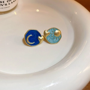Detail of asymmetric enamel stud earrings featuring sun and moon motifs on a white plate