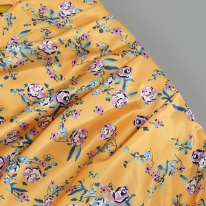 Close-up of yellow satin fabric featuring purple floral print and elegant silky drapes