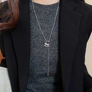 Close-up of a silver rocking horse pendant necklace on a dark sweater for premium styling