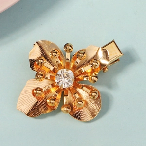 Golden clover hair clip with clear rhinestone center on a light blue matte background