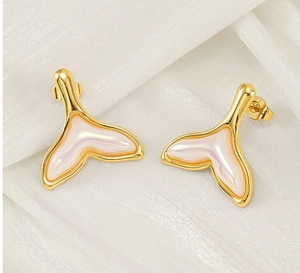 Détail macro de boucles d'oreilles queue de sirène dorées sur fond en soie blanche élégante