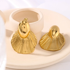 Minimalist gold fan-shaped leaf earrings with textured metallic finish on ceramic stand