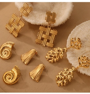 Detailed view of gold plated sea conch and woven geometric earrings on white coral decor