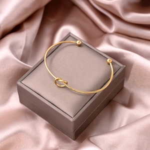 Detail of gold knot open cuff bracelet with spherical ends on silk and jewelry box