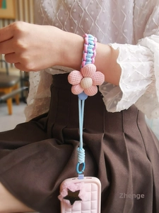 Close-up of pink fabric flower and woven pastel phone lanyard on a hand