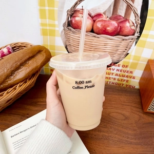 Hand hält klaren Plastik-Kaffeebecher mit Strohhalm in gemütlicher Café-Atmosphäre