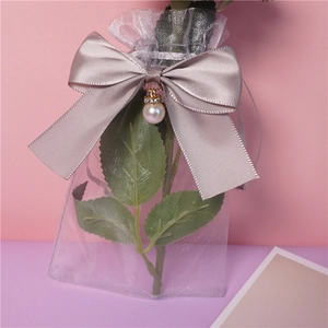 Detail of gray organza gift bag with ribbon bow and elegant pearl pendant accent