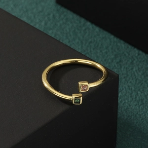 Adjustable gold open ring featuring elegant green and pink square gemstones on black stand