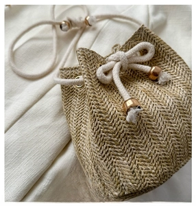 Detail of woven straw bucket bag showing tight herringbone pattern and golden cord lock