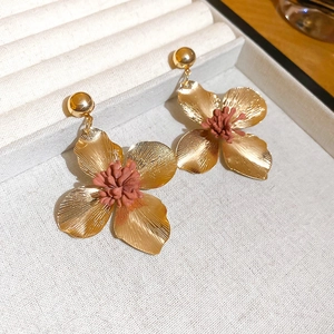 Close-up of golden flower earrings with pink stamen on a beige jewelry display tray
