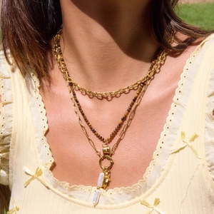 Detail of layered gold titanium necklace featuring beads and bar pendant on neck