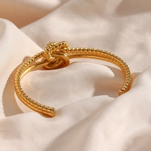 Elegant gold knot cuff bracelet with twisted rope design on white silk background