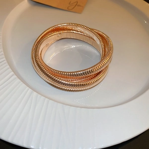 Detail of three-tier elastic spiral gold bangle on a white ceramic display tray