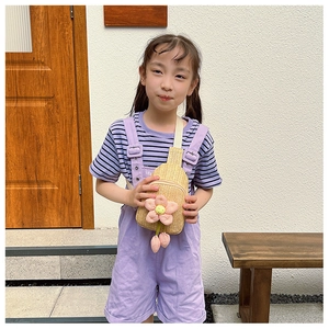 Close-up of children's hand-woven straw chest bag with pink flower detail and purple strap