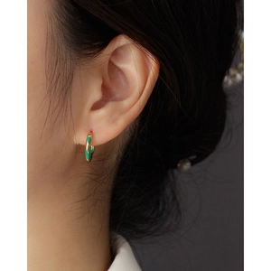 Close-up of a gold-plated hoop earring with green enamel spiral texture on a model's ear